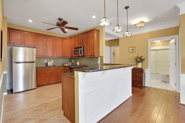 kitchen with stainless steel appliances, brown cabinetry, dark stone counters, a peninsula, and a kitchen bar