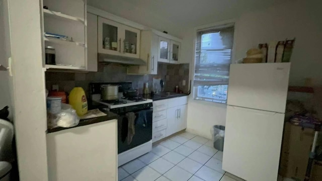 kitchen with range with gas stovetop, glass insert cabinets, freestanding refrigerator, white cabinets, and under cabinet range hood