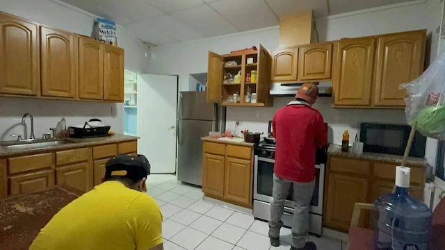 kitchen featuring light tile patterned floors, glass insert cabinets, appliances with stainless steel finishes, under cabinet range hood, and a sink