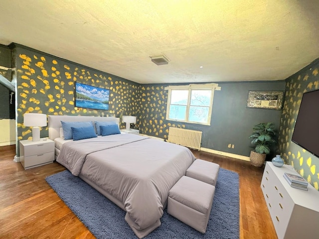 bedroom with wallpapered walls, radiator heating unit, wood finished floors, and baseboards