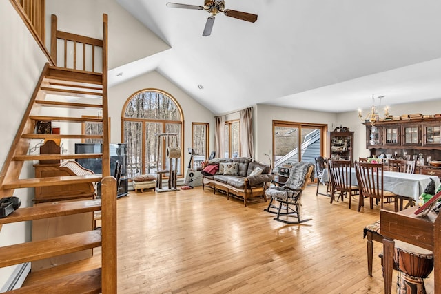 living area with ceiling fan with notable chandelier, high vaulted ceiling, stairway, and wood finished floors