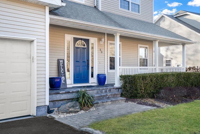 entrance to property with a porch, roof with shingles, and an attached garage