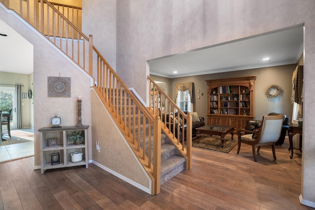 stairs featuring a towering ceiling, wood-type flooring, baseboards, and crown molding