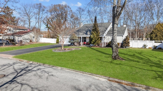 view of front facade with driveway, a garage, a chimney, fence, and a front lawn