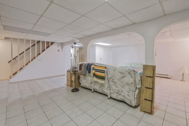 living area featuring stairs, arched walkways, a drop ceiling, and a baseboard radiator