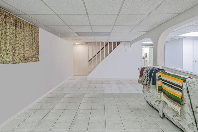 finished basement with arched walkways, a drop ceiling, baseboards, and stairs