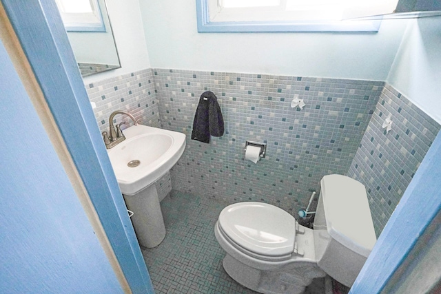 bathroom featuring tile patterned flooring, toilet, a wainscoted wall, a sink, and tile walls