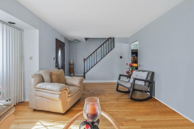 living area featuring light wood-style floors, baseboards, and stairs