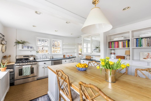 kitchen with stainless steel appliances, a sink, white cabinets, hanging light fixtures, and open shelves