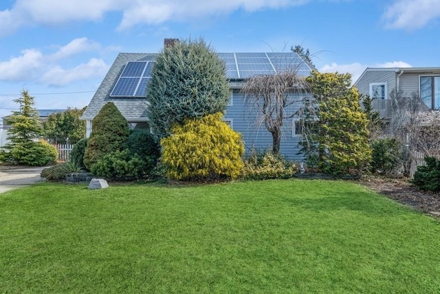 view of side of property featuring a yard, a shingled roof, and solar panels