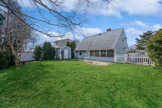 rear view of property featuring a storage shed, a shingled roof, a yard, fence, and an outdoor structure