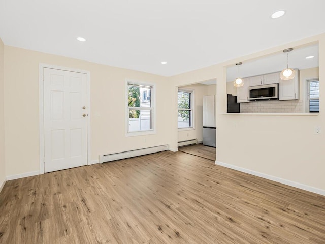 unfurnished living room with a baseboard heating unit, baseboards, a wealth of natural light, and light wood-style floors