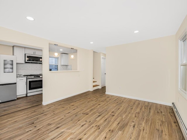 interior space with light countertops, decorative backsplash, baseboard heating, freestanding refrigerator, and stainless steel range with gas stovetop