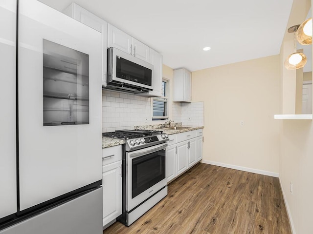 kitchen with light stone counters, refrigerator, white cabinetry, backsplash, and gas stove