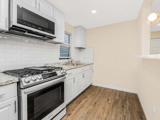 kitchen with stainless steel gas stove, a sink, white cabinetry, and light stone countertops