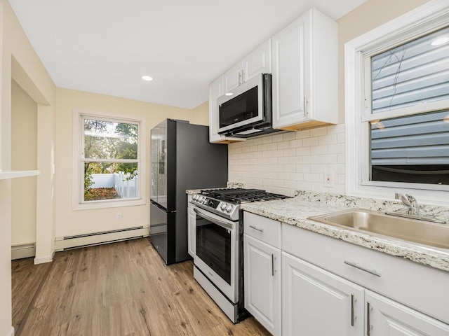 kitchen featuring a baseboard heating unit, appliances with stainless steel finishes, white cabinets, and a sink