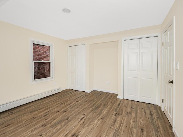 unfurnished bedroom featuring multiple closets, a baseboard radiator, baseboards, and dark wood-style floors