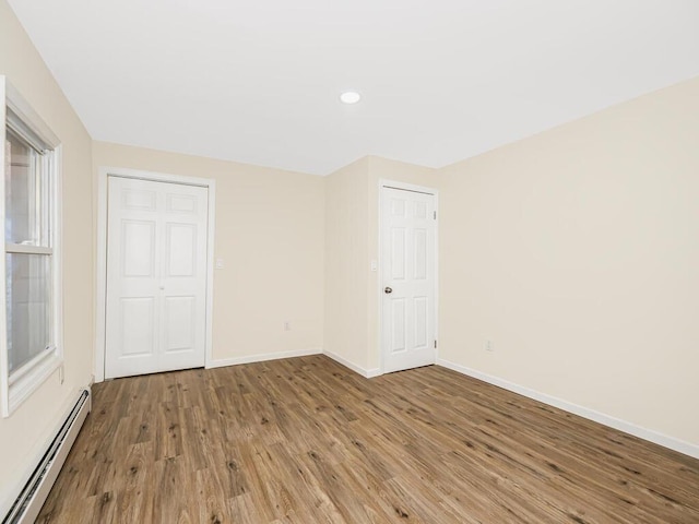 empty room with baseboards, baseboard heating, wood finished floors, and recessed lighting