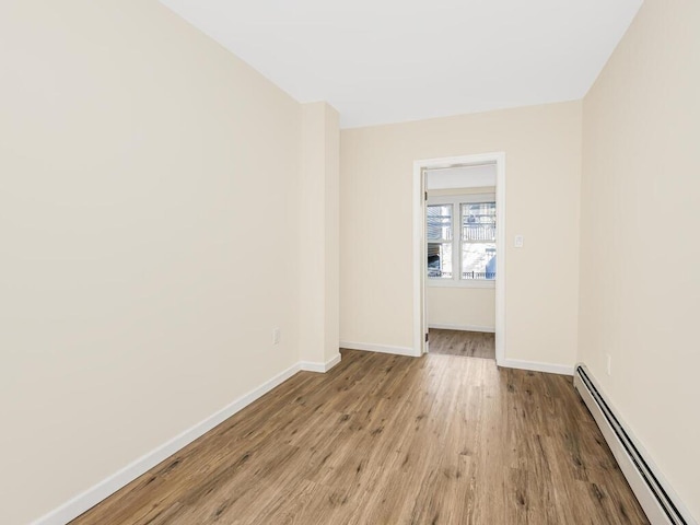 unfurnished room with a baseboard heating unit, baseboards, and light wood finished floors