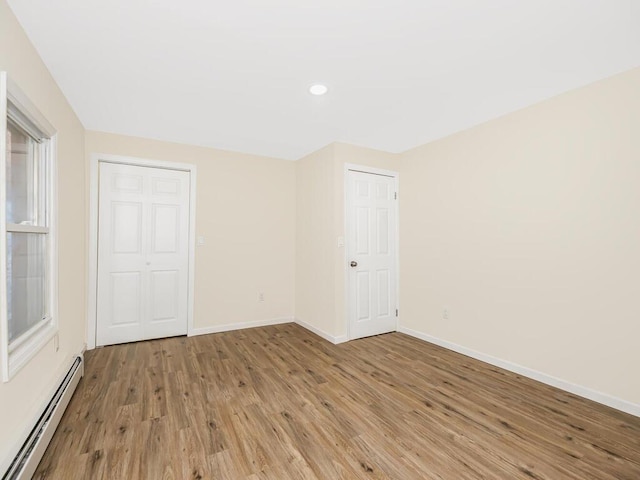 unfurnished bedroom with a baseboard heating unit, baseboards, and light wood finished floors