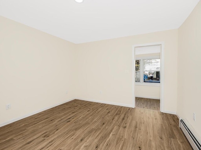 spare room featuring a baseboard radiator, wood finished floors, and baseboards