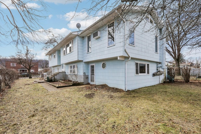 rear view of house featuring a yard, a wall unit AC, and fence