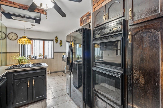 kitchen featuring ceiling fan, a wainscoted wall, wood walls, black appliances, and decorative light fixtures