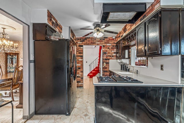 kitchen with brick wall, stovetop with downdraft, freestanding refrigerator, a sink, and ceiling fan with notable chandelier