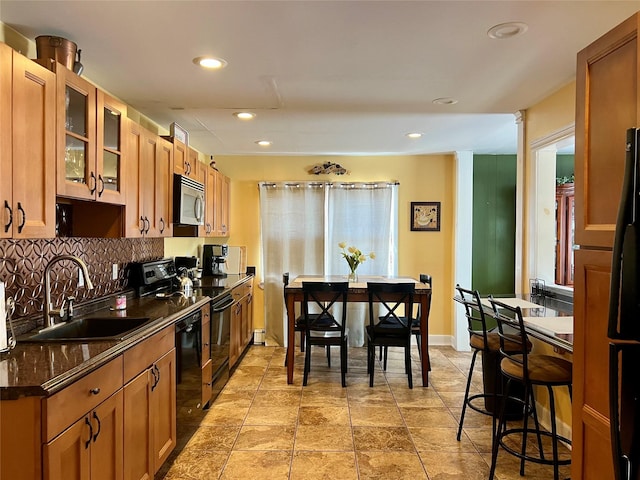 kitchen featuring black appliances, a sink, glass insert cabinets, brown cabinetry, and decorative backsplash