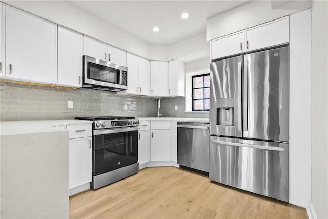 kitchen featuring light countertops, light wood-style flooring, decorative backsplash, appliances with stainless steel finishes, and white cabinets