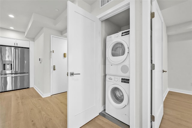 laundry area featuring laundry area, stacked washer / dryer, visible vents, and light wood-style floors