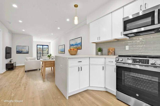 kitchen featuring light wood finished floors, light countertops, hanging light fixtures, appliances with stainless steel finishes, and open floor plan