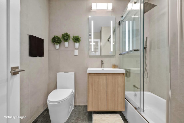 full bath with tile walls, shower / bath combination with glass door, vanity, and toilet