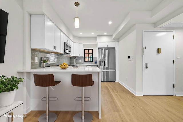 kitchen with light countertops, tasteful backsplash, light wood-type flooring, stainless steel appliances, and a peninsula