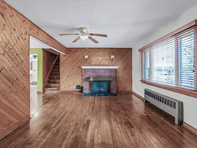 unfurnished living room featuring stairs, radiator heating unit, a fireplace, and hardwood / wood-style flooring