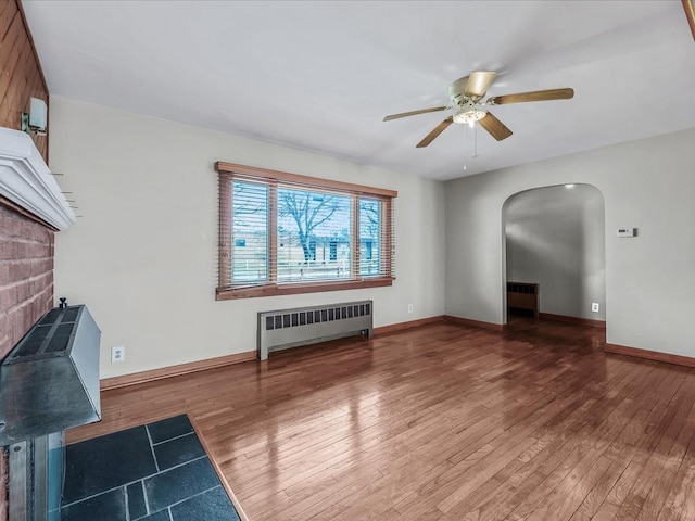 unfurnished living room featuring arched walkways, hardwood / wood-style floors, and radiator heating unit