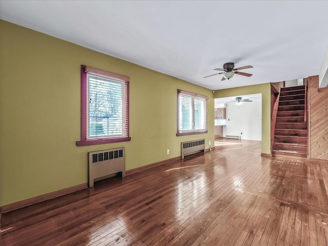 unfurnished living room with stairway, radiator, wood-type flooring, and baseboards