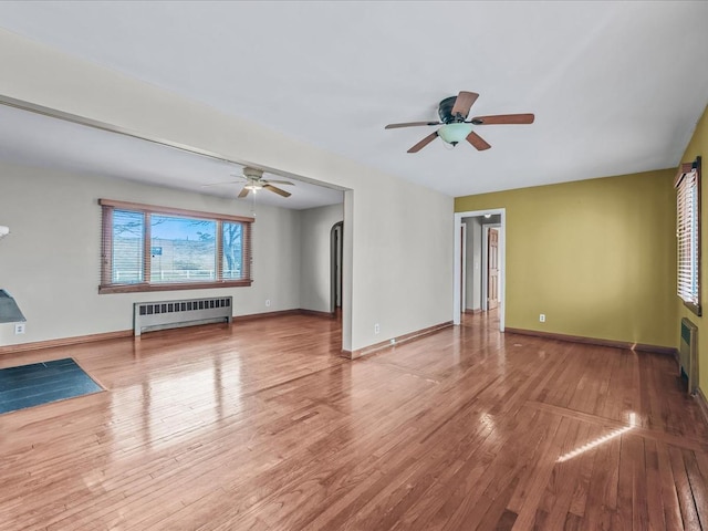 unfurnished living room with a ceiling fan, radiator heating unit, baseboards, and wood finished floors