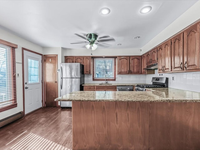 kitchen with light stone counters, under cabinet range hood, stainless steel appliances, a peninsula, and a sink