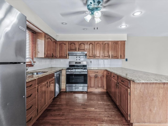 kitchen with dark wood finished floors, appliances with stainless steel finishes, a peninsula, under cabinet range hood, and a sink