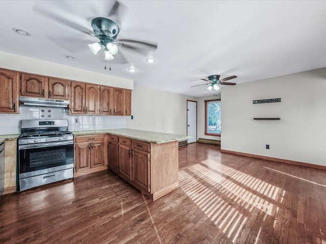 kitchen featuring baseboards, dark wood-style floors, a peninsula, under cabinet range hood, and stainless steel range with gas stovetop