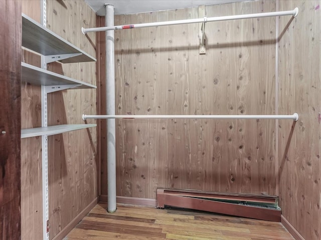 spacious closet with a baseboard heating unit and wood finished floors