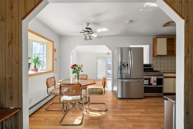 dining room featuring ceiling fan, light wood-style flooring, a baseboard heating unit, and arched walkways