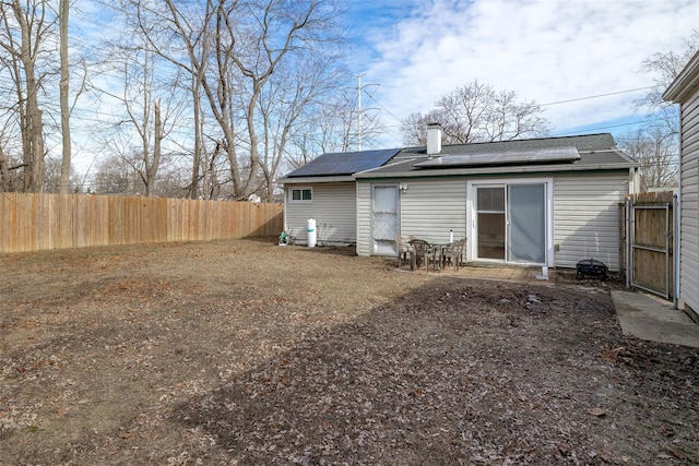 rear view of property with a fenced backyard, roof mounted solar panels, and a chimney