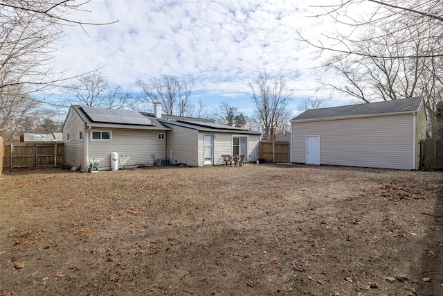 rear view of property featuring fence private yard, a chimney, roof mounted solar panels, and central AC unit