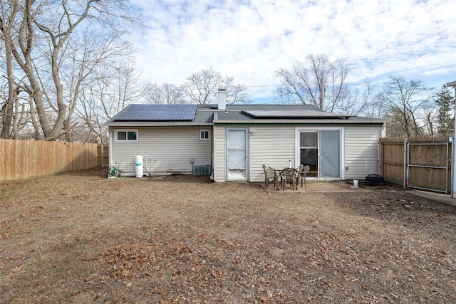 rear view of property featuring a fenced backyard, roof mounted solar panels, and cooling unit