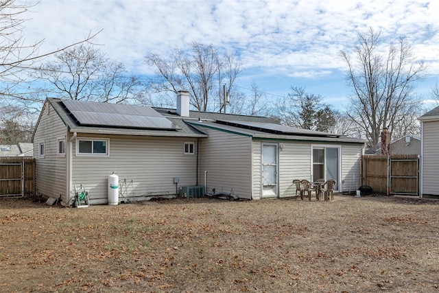 back of house with roof mounted solar panels, central AC, fence, and a chimney