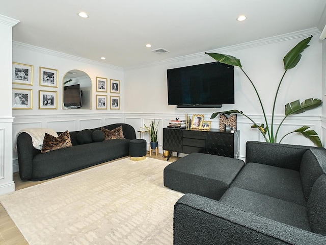 living room with a decorative wall, wainscoting, visible vents, and crown molding