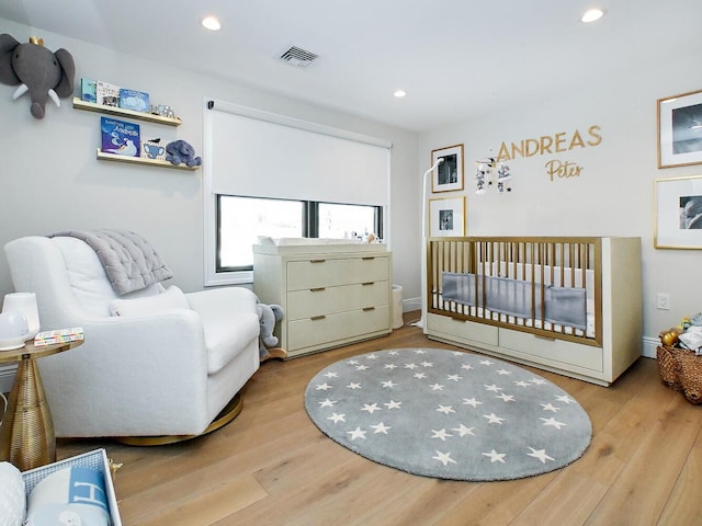 bedroom with a nursery area, visible vents, wood finished floors, and recessed lighting