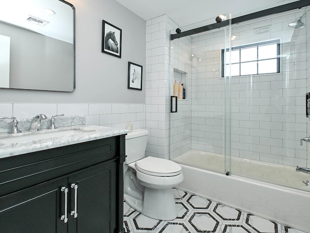 bathroom with toilet, bath / shower combo with glass door, vanity, visible vents, and tile walls